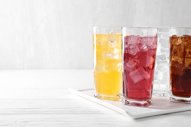 Photo of Soda water of different flavors with ice cubes in glasses on white wooden table, space for text