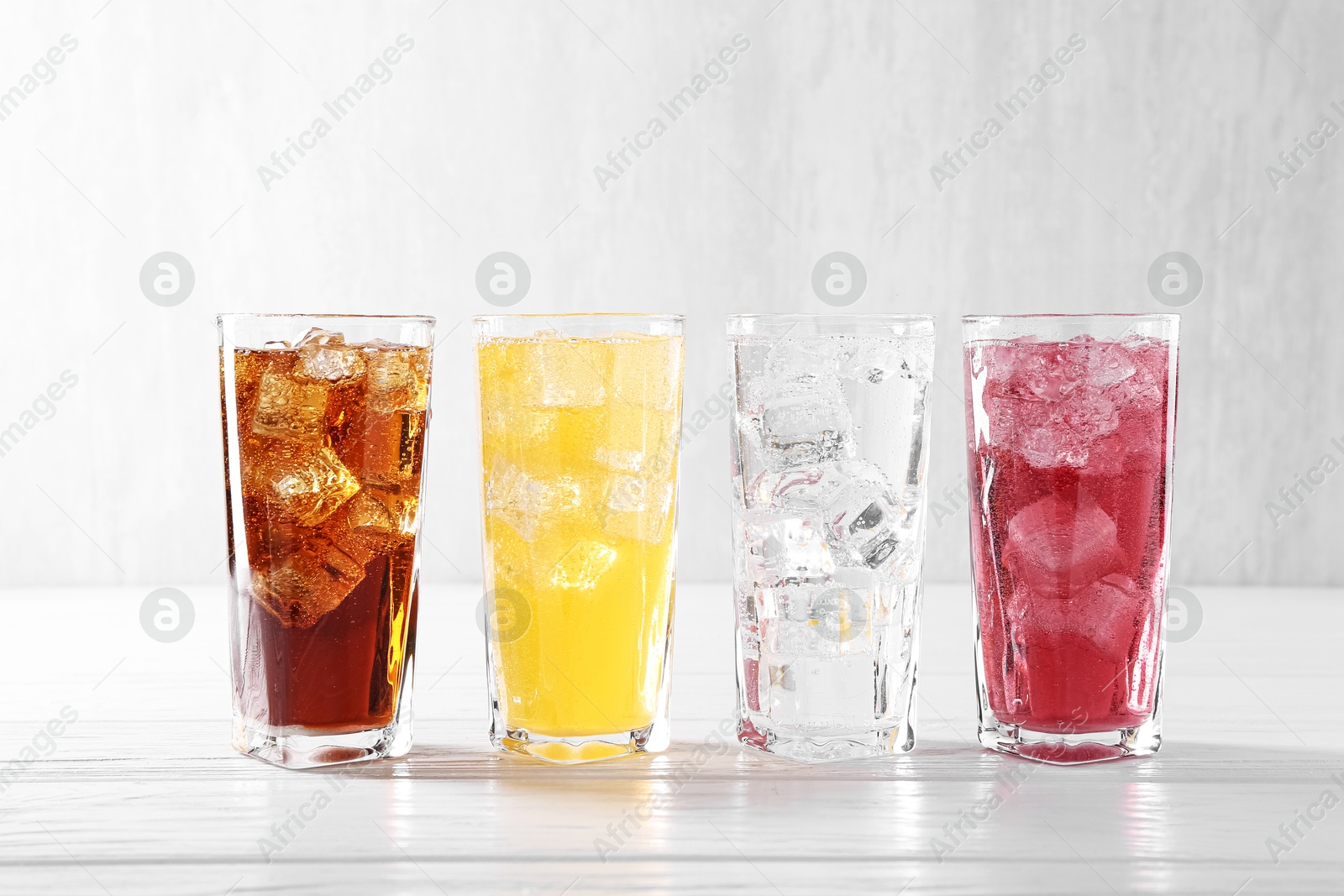 Photo of Soda water of different flavors with ice cubes in glasses on white wooden table