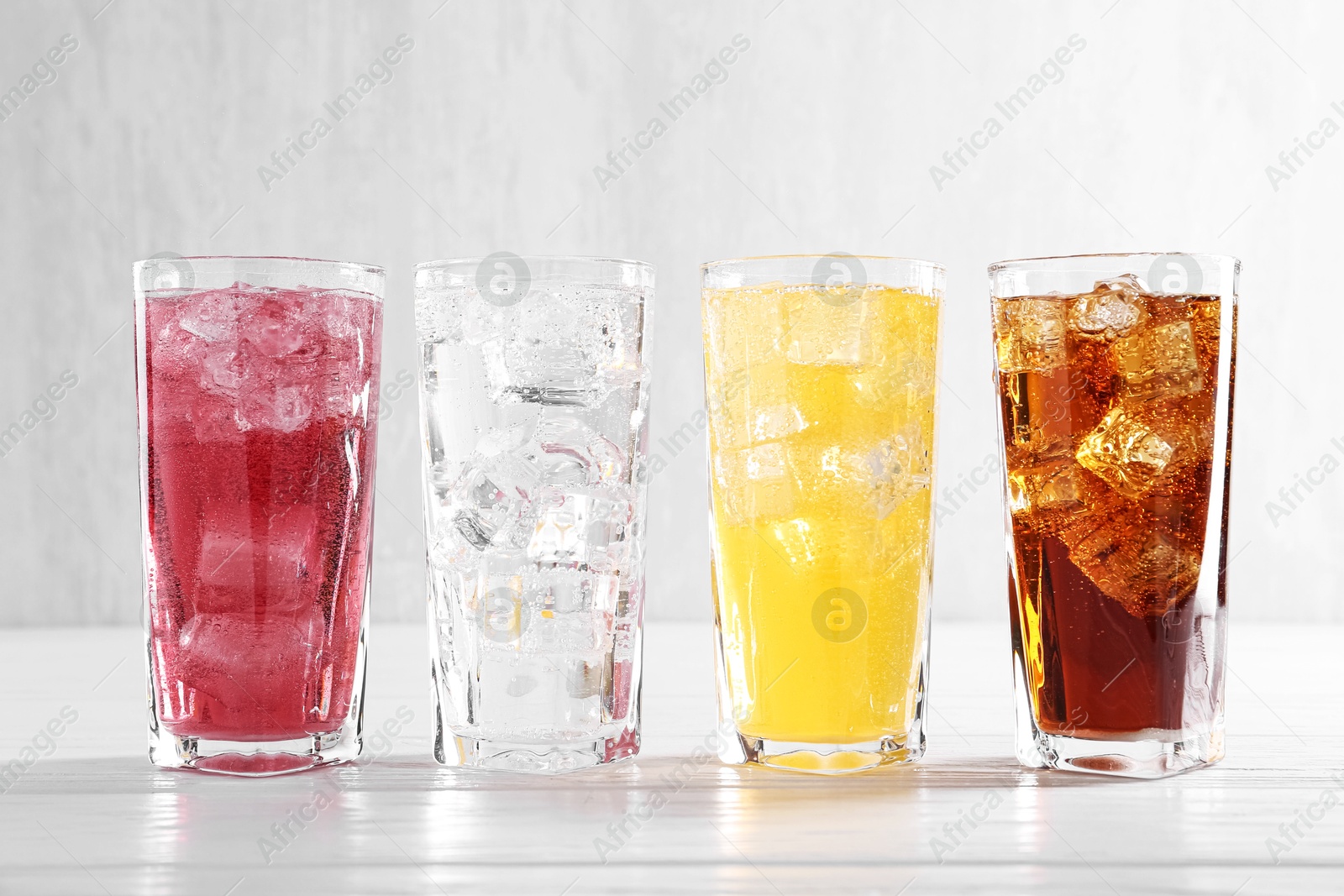 Photo of Soda water of different flavors with ice cubes in glasses on white wooden table