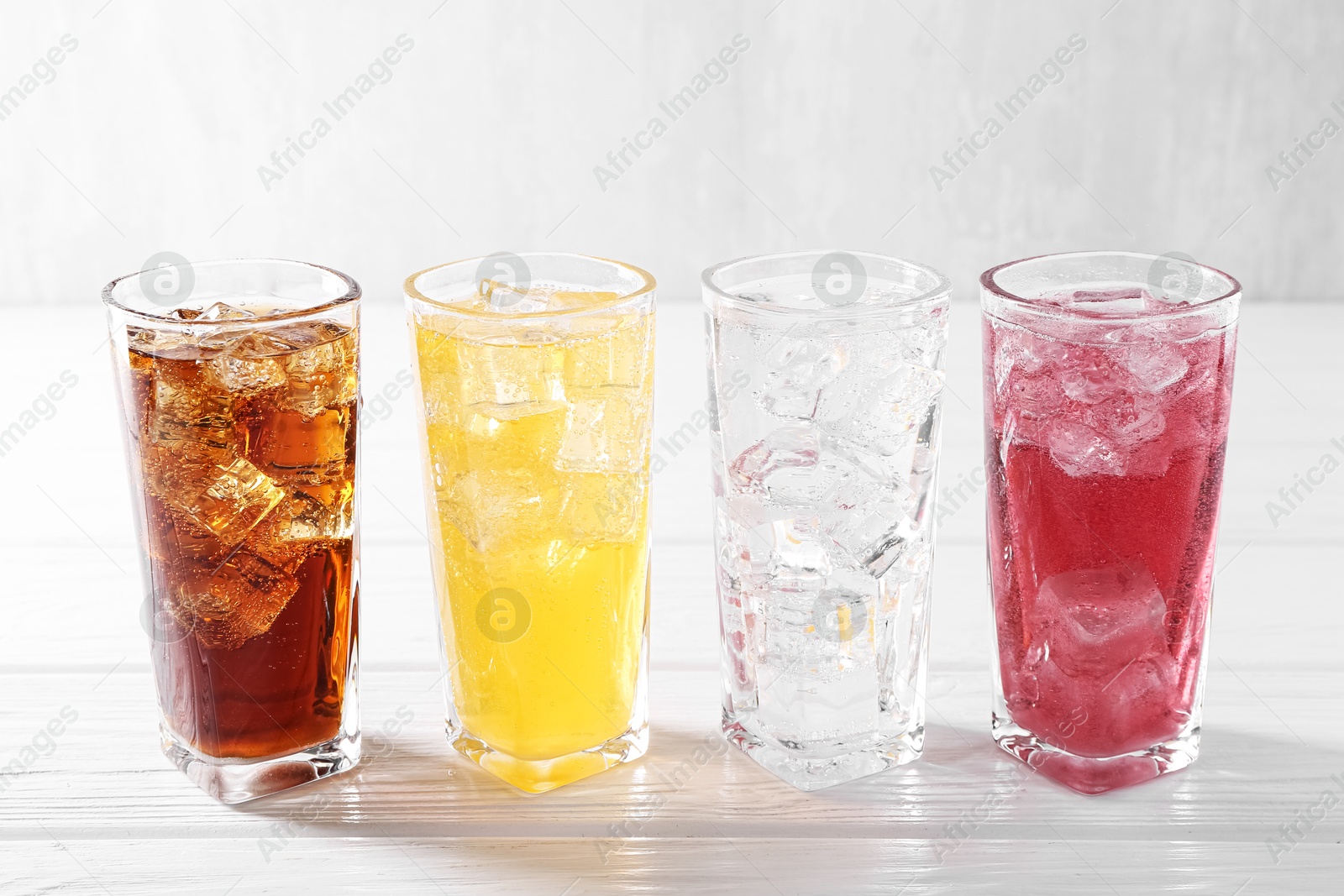 Photo of Soda water of different flavors with ice cubes in glasses on white wooden table