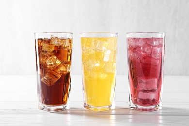 Photo of Soda water of different flavors with ice cubes in glasses on white wooden table