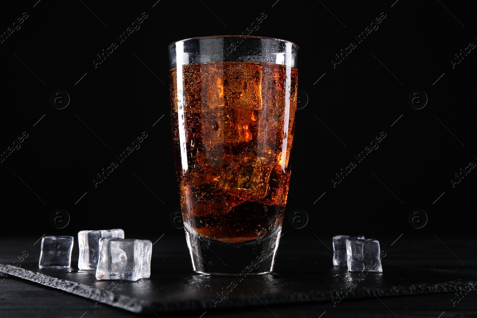 Photo of Sweet soda water in glass with ice cubes on black wooden table, closeup