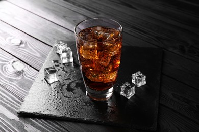 Photo of Sweet soda water in glass with ice cubes on black wooden table