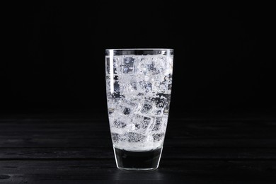 Photo of Refreshing soda water with ice cubes in glass on black wooden table