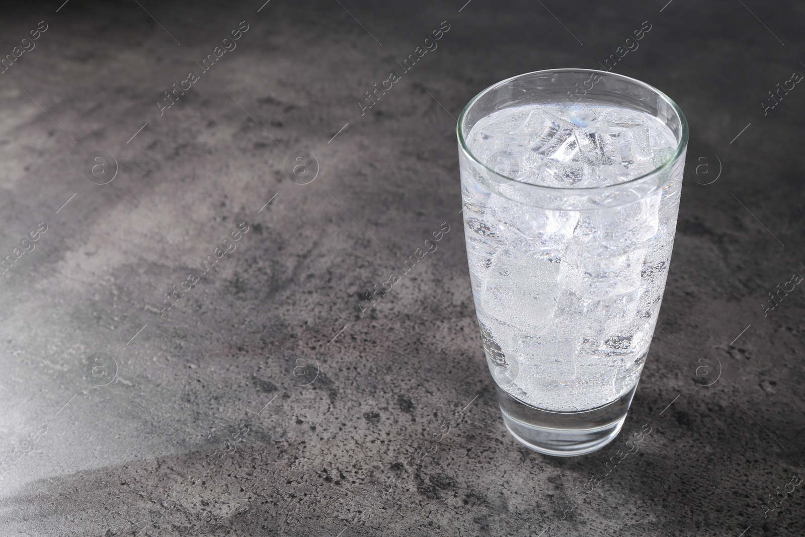 Photo of Refreshing soda water with ice cubes in glass on grey table, space for text