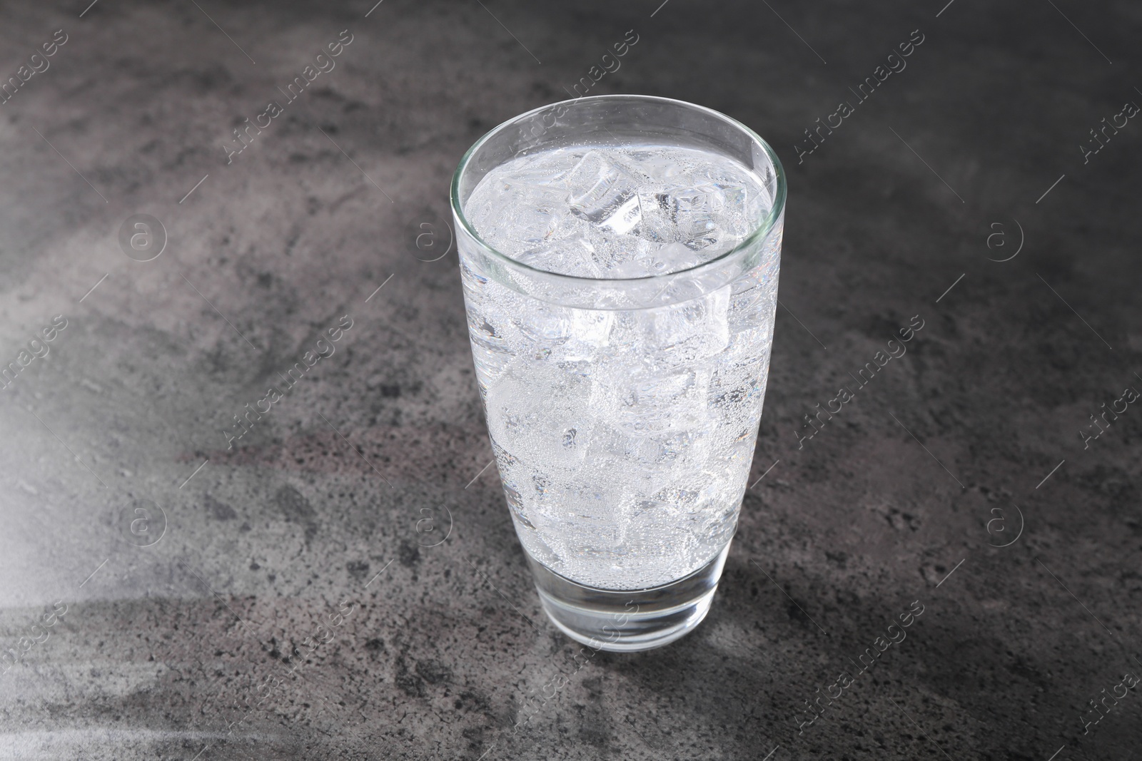 Photo of Refreshing soda water with ice cubes in glass on grey table