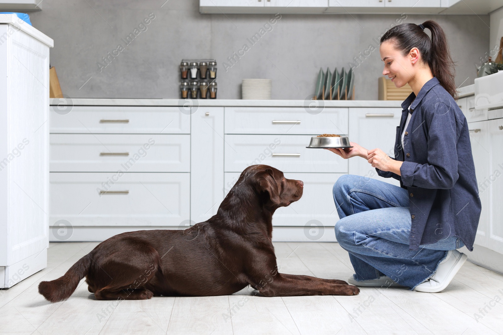 Photo of Woman giving bowl with dry pet food to her dog indoors