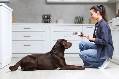 Photo of Woman giving bowl with dry pet food to her dog indoors