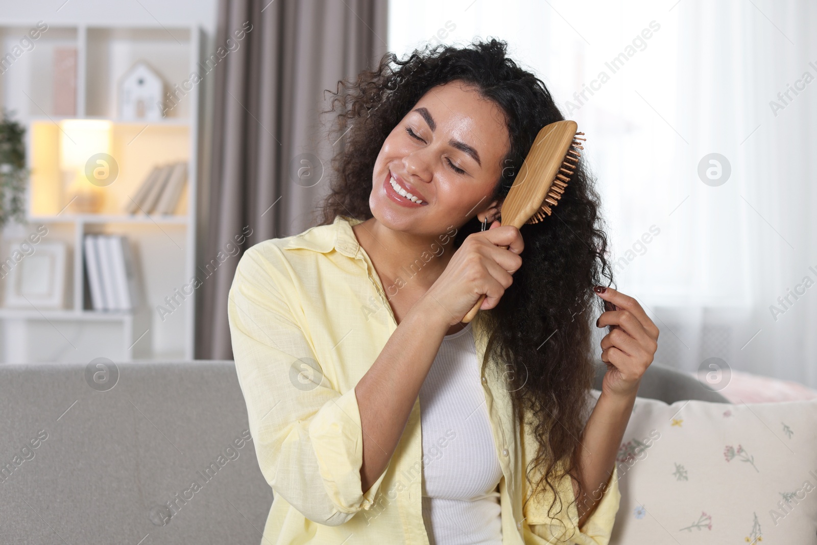 Photo of Smiling young woman brushing her curly hair at home