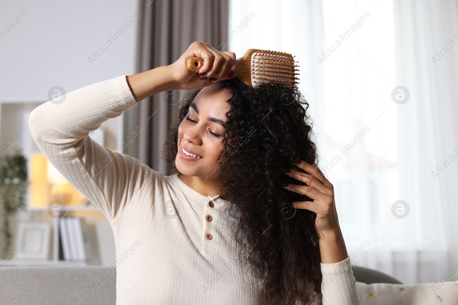 Photo of Smiling young woman brushing her curly hair at home