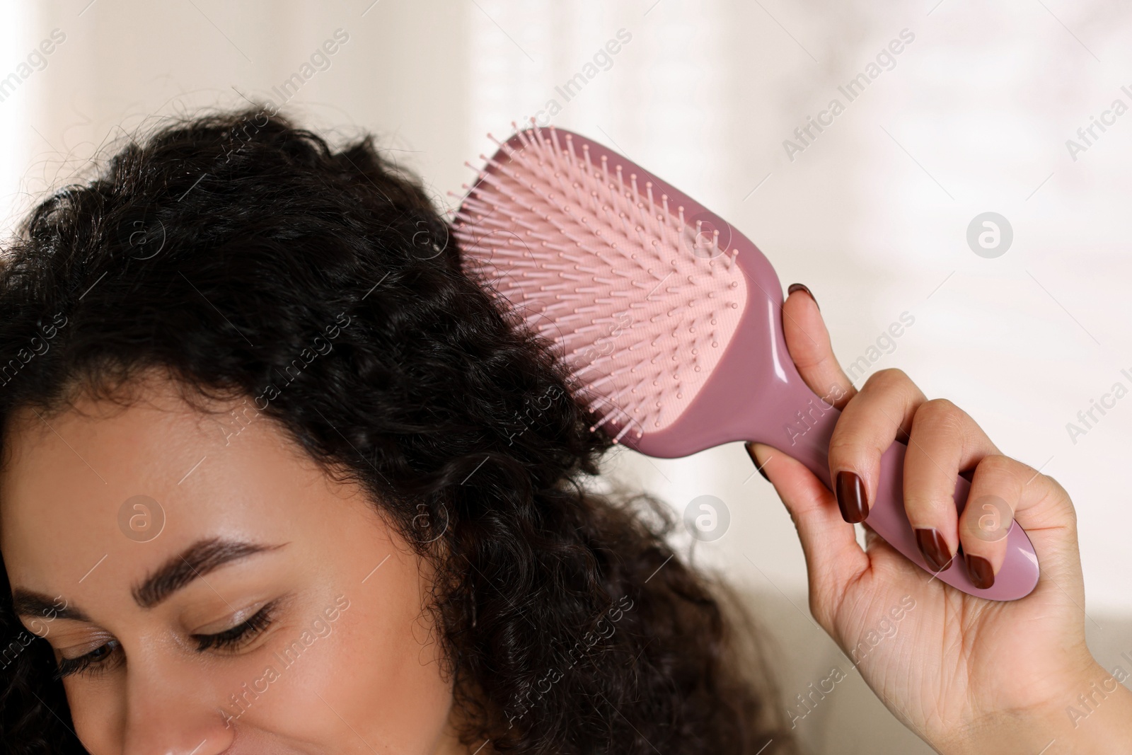 Photo of Woman brushing her curly hair indoors, closeup