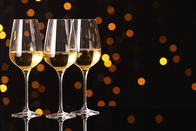 Photo of Tasty white wine in glasses on mirror surface against dark background with blurred lights, space for text. Bokeh effect