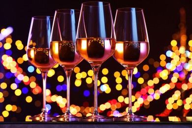 Photo of Tasty white wine in glasses against black background with blurred lights, bokeh effect