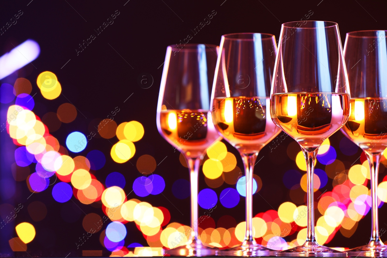 Photo of Tasty white wine in glasses against dark background with blurred lights, space for text. Bokeh effect