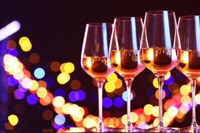 Photo of Tasty white wine in glasses against dark background with blurred lights, space for text. Bokeh effect