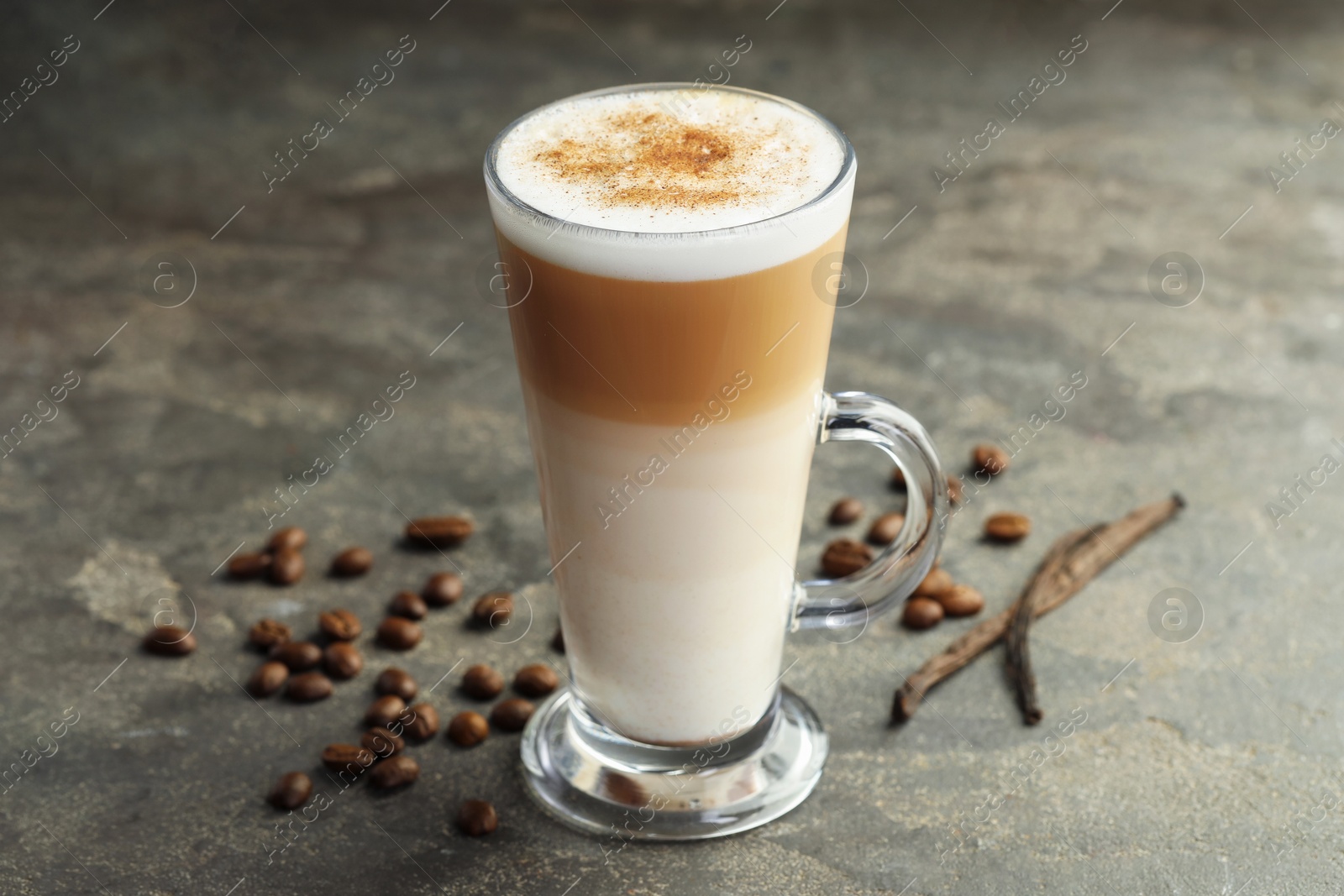 Photo of Tasty latte macchiato in glass cup, coffee beans and vanilla pods on grey table, closeup