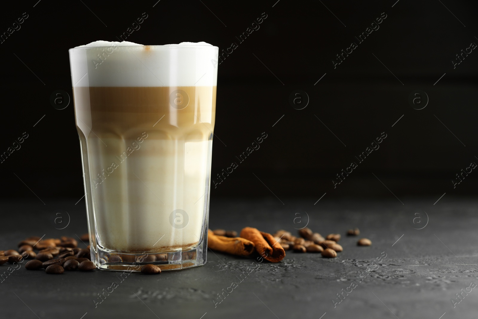 Photo of Tasty latte macchiato in glass, coffee beans and cinnamon on black table, closeup. Space for text