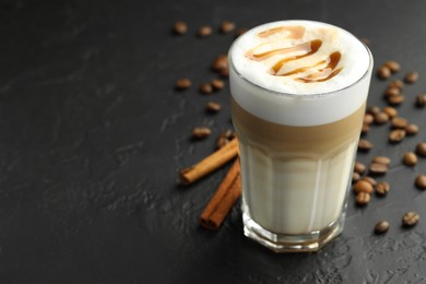 Photo of Tasty latte macchiato in glass, coffee beans and cinnamon on black table, closeup. Space for text