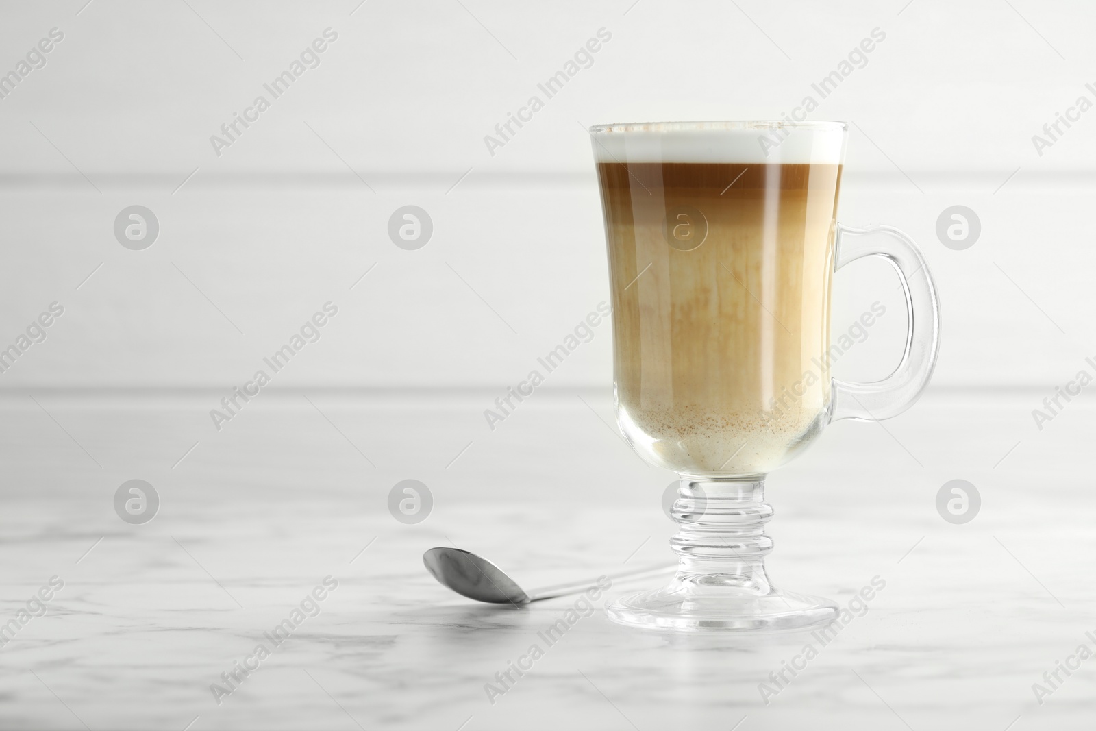 Photo of Tasty latte macchiato in glass cup on white marble table, closeup. Space for text