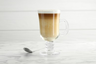 Photo of Tasty latte macchiato in glass cup on white marble table, closeup