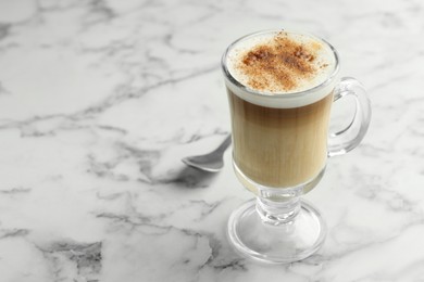 Photo of Tasty latte macchiato in glass cup on white marble table, closeup. Space for text