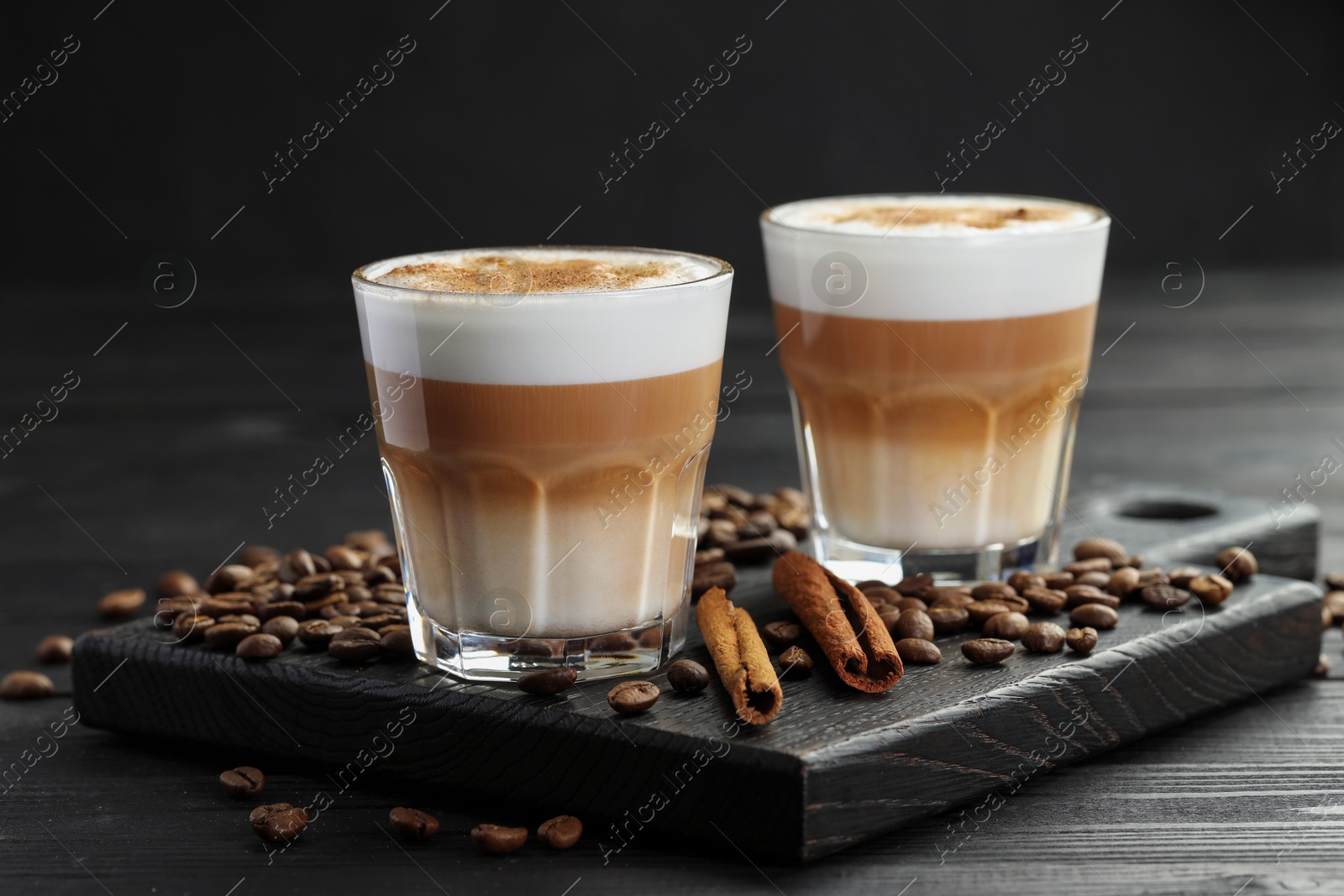 Photo of Tasty latte macchiato in glasses, coffee beans and cinnamon on black wooden table, closeup