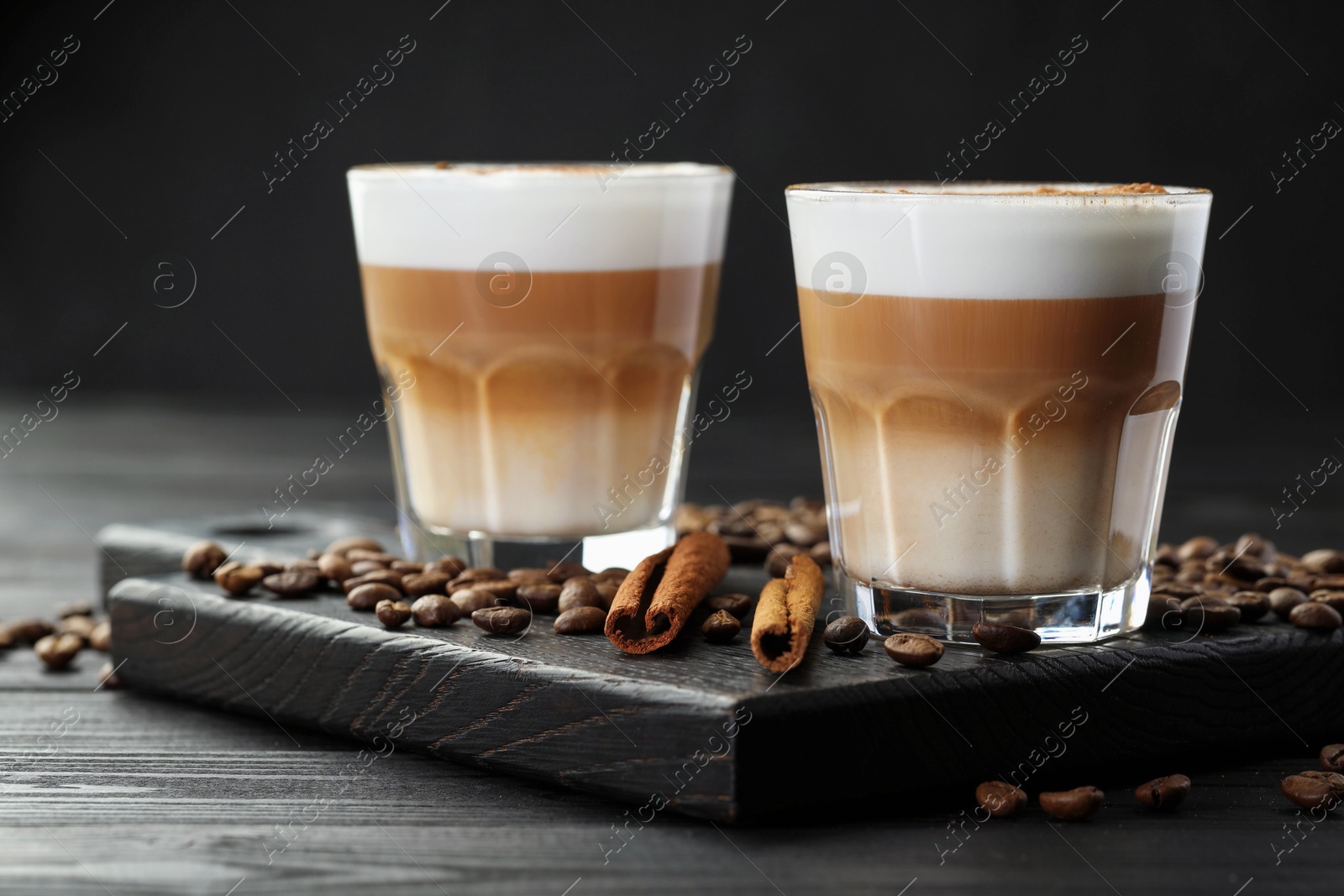 Photo of Tasty latte macchiato in glasses, coffee beans and cinnamon on black wooden table, closeup