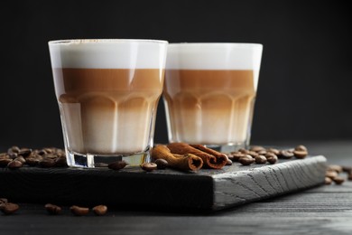 Photo of Tasty latte macchiato in glasses, coffee beans and cinnamon on black wooden table, closeup