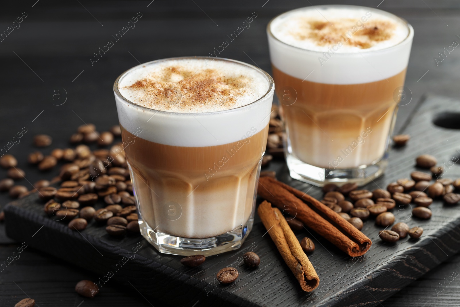 Photo of Tasty latte macchiato in glasses, coffee beans and cinnamon on black wooden table, closeup