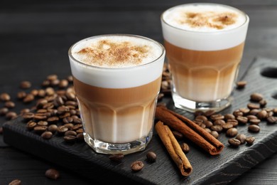 Photo of Tasty latte macchiato in glasses, coffee beans and cinnamon on black wooden table, closeup