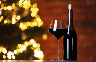 Photo of Tasty red wine in glass and bottle on table against blurred lights, space for text. Bokeh effect