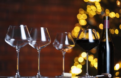 Photo of Glass with red wine and empty ones on table against blurred lights. Bokeh effect