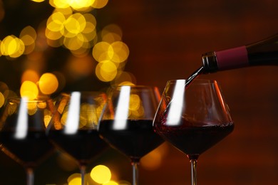 Photo of Pouring red wine into glass against blurred lights, closeup. Bokeh effect