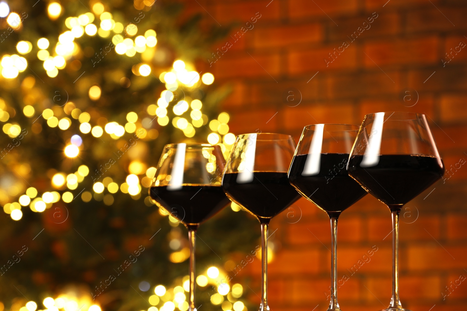 Photo of Tasty red wine in glasses on table against blurred lights, space for text. Bokeh effect