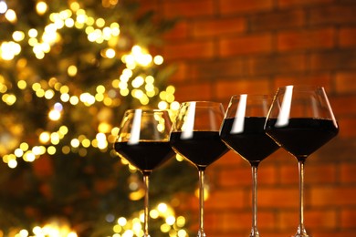 Photo of Tasty red wine in glasses on table against blurred lights, space for text. Bokeh effect