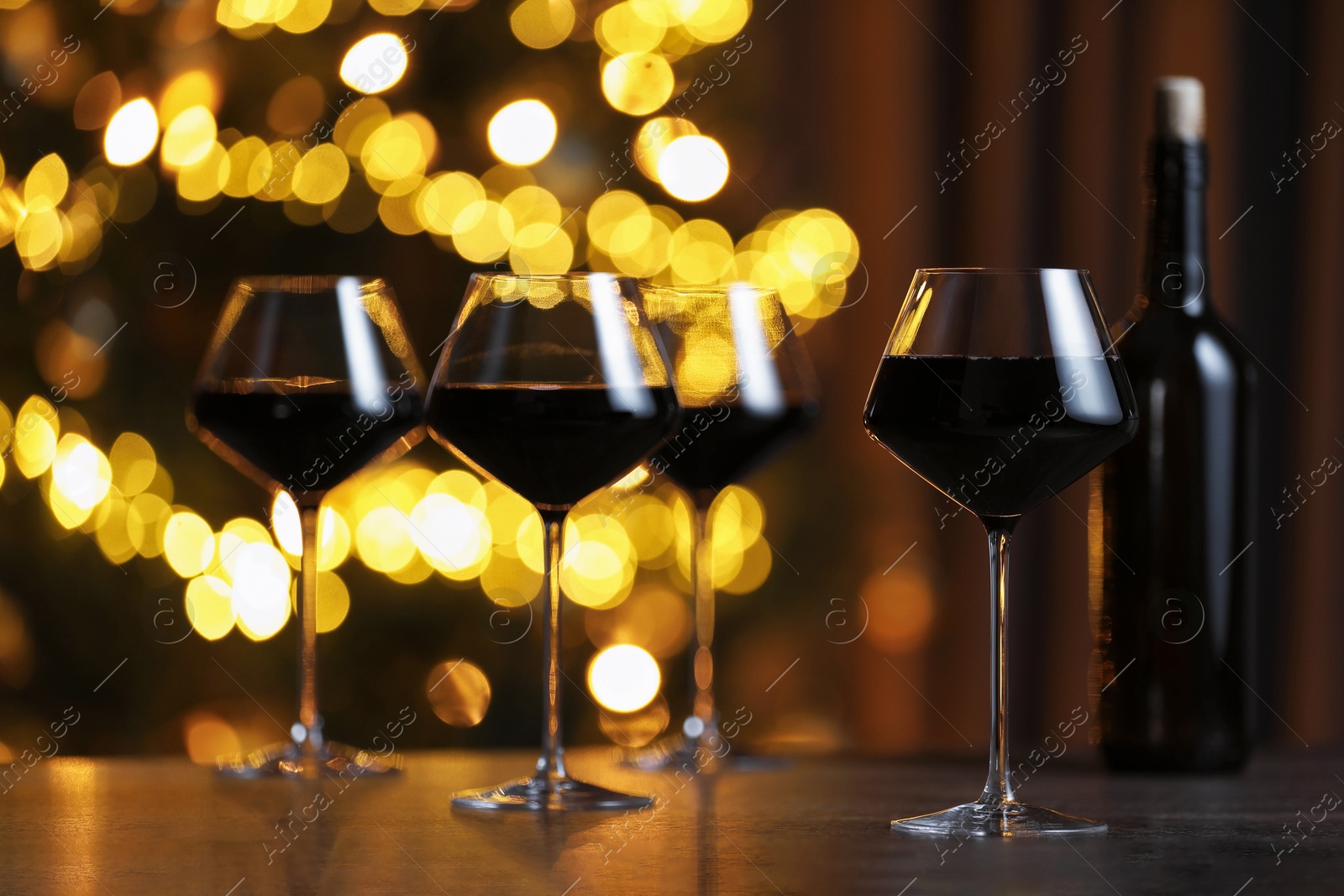 Photo of Tasty red wine in glasses on table against blurred lights. Bokeh effect