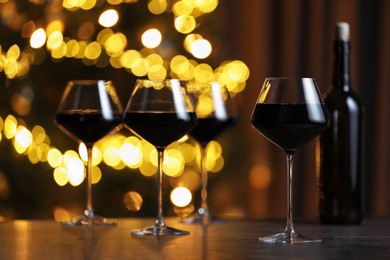 Photo of Tasty red wine in glasses on table against blurred lights. Bokeh effect