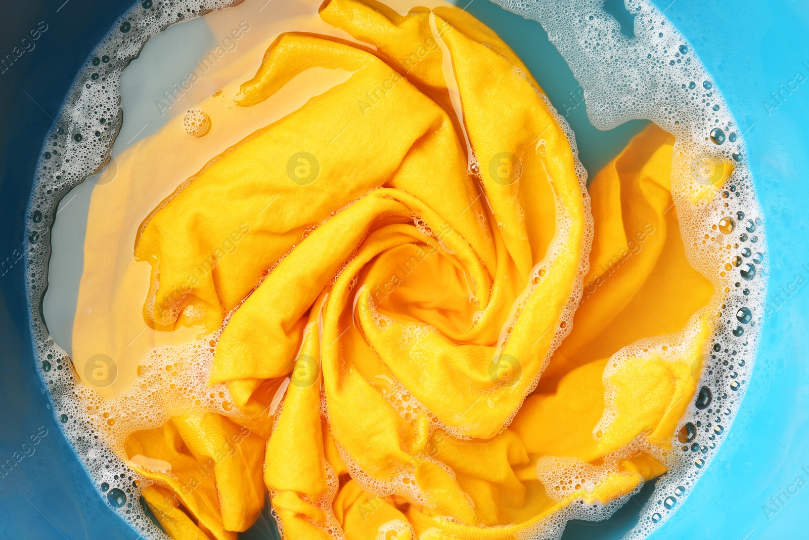 Photo of Yellow clothes soaked in water before washing, top view