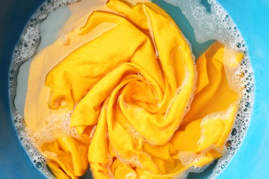 Photo of Yellow clothes soaked in water before washing, top view