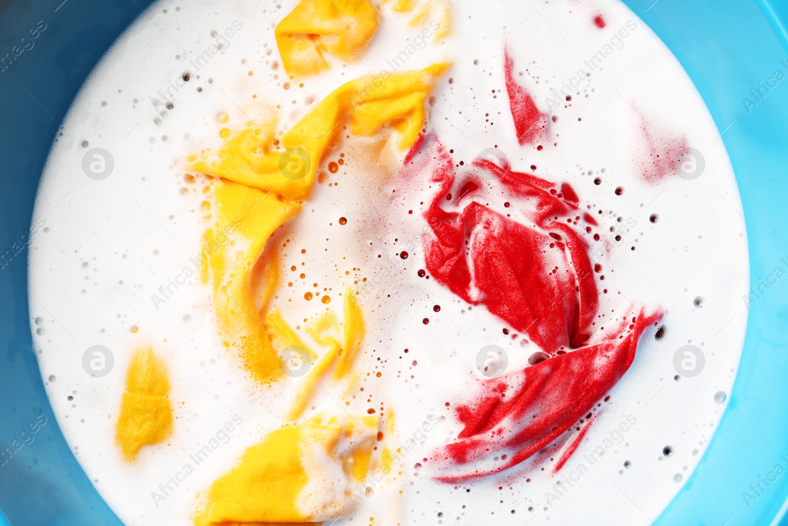 Photo of Colorful clothes soaked in water before washing, top view