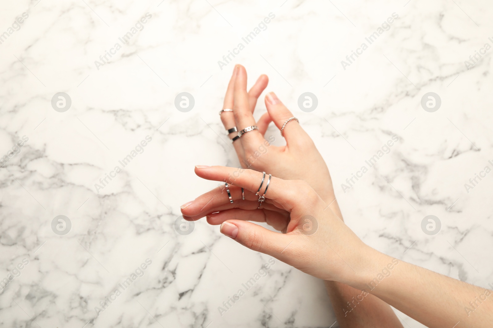 Photo of Woman wearing beautiful rings at white marble table, top view. Space for text