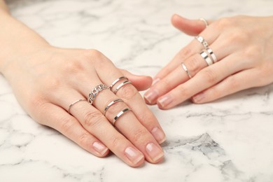 Woman wearing beautiful rings at white marble table, closeup