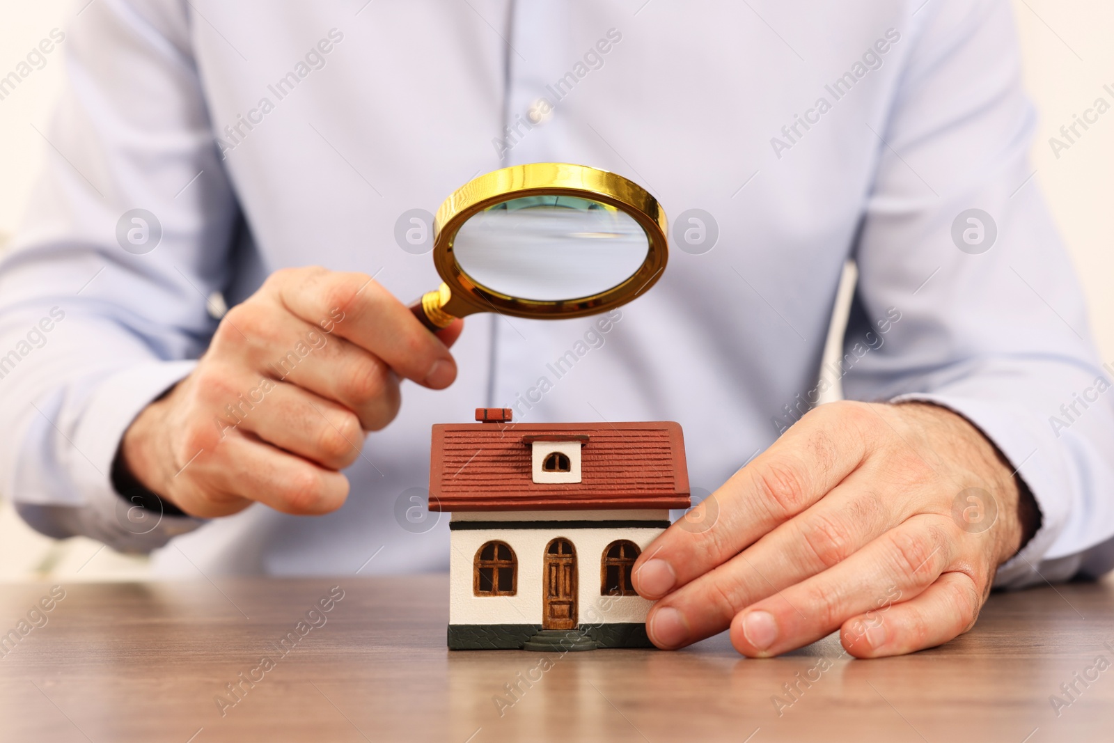 Photo of Real estate agent looking at house figure through magnifying glass at wooden table in office, closeup. Home appraisal