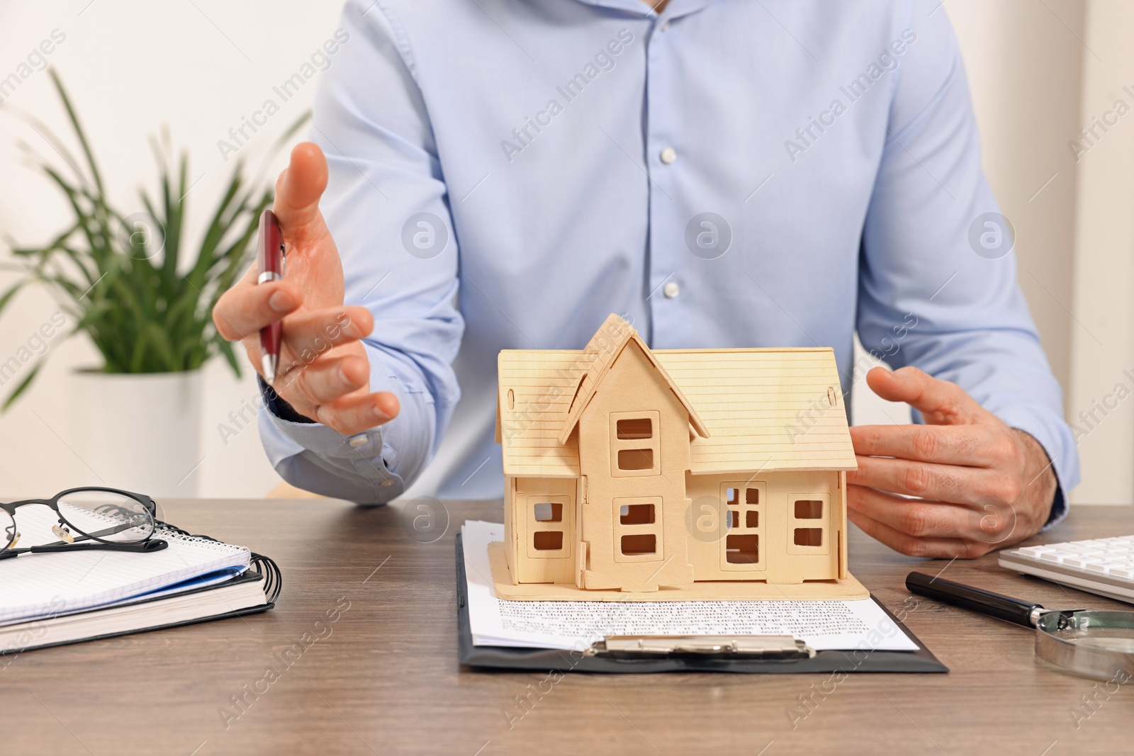 Photo of Real estate agent at wooden table with house figure and documents in office, closeup. Home appraisal