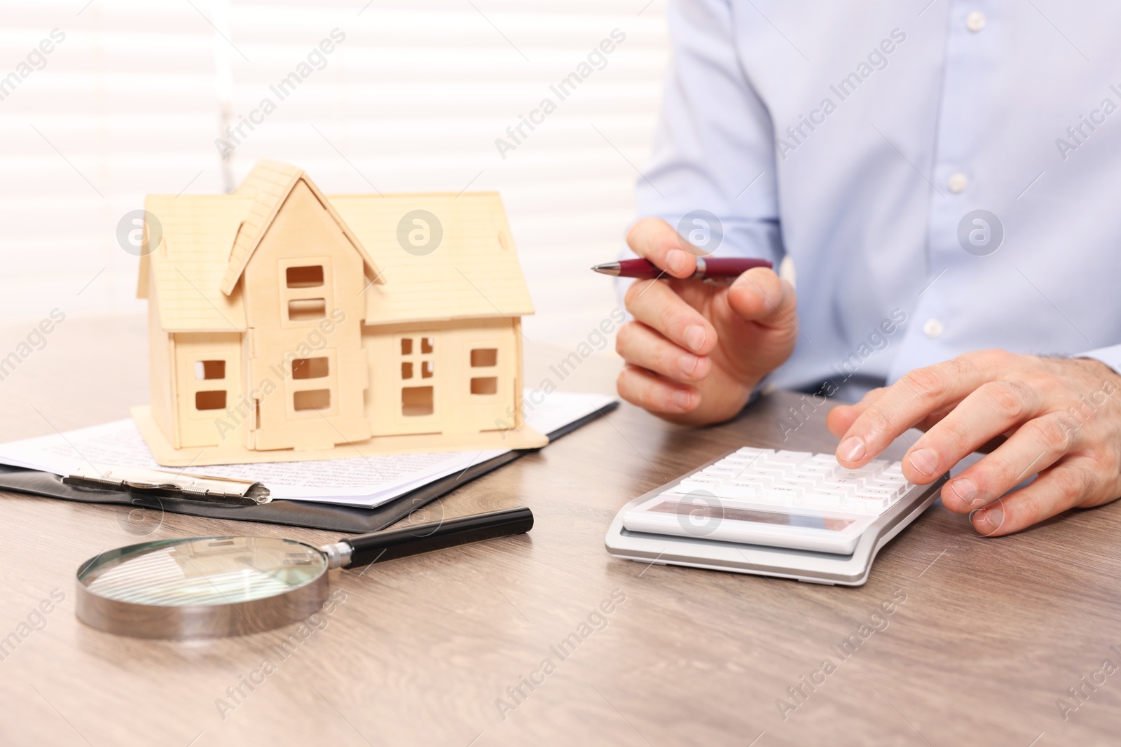 Photo of Real estate agent with calculator at wooden table in office, closeup. Home appraisal