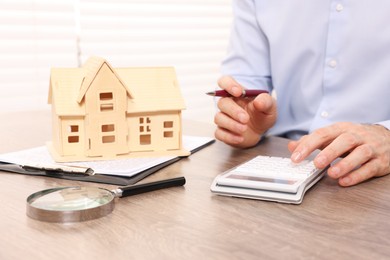 Real estate agent with calculator at wooden table in office, closeup. Home appraisal