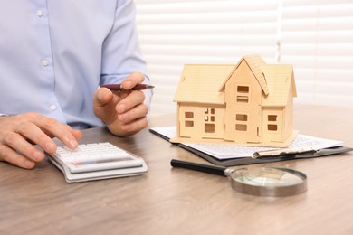 Photo of Real estate agent with calculator at wooden table in office, closeup. Home appraisal