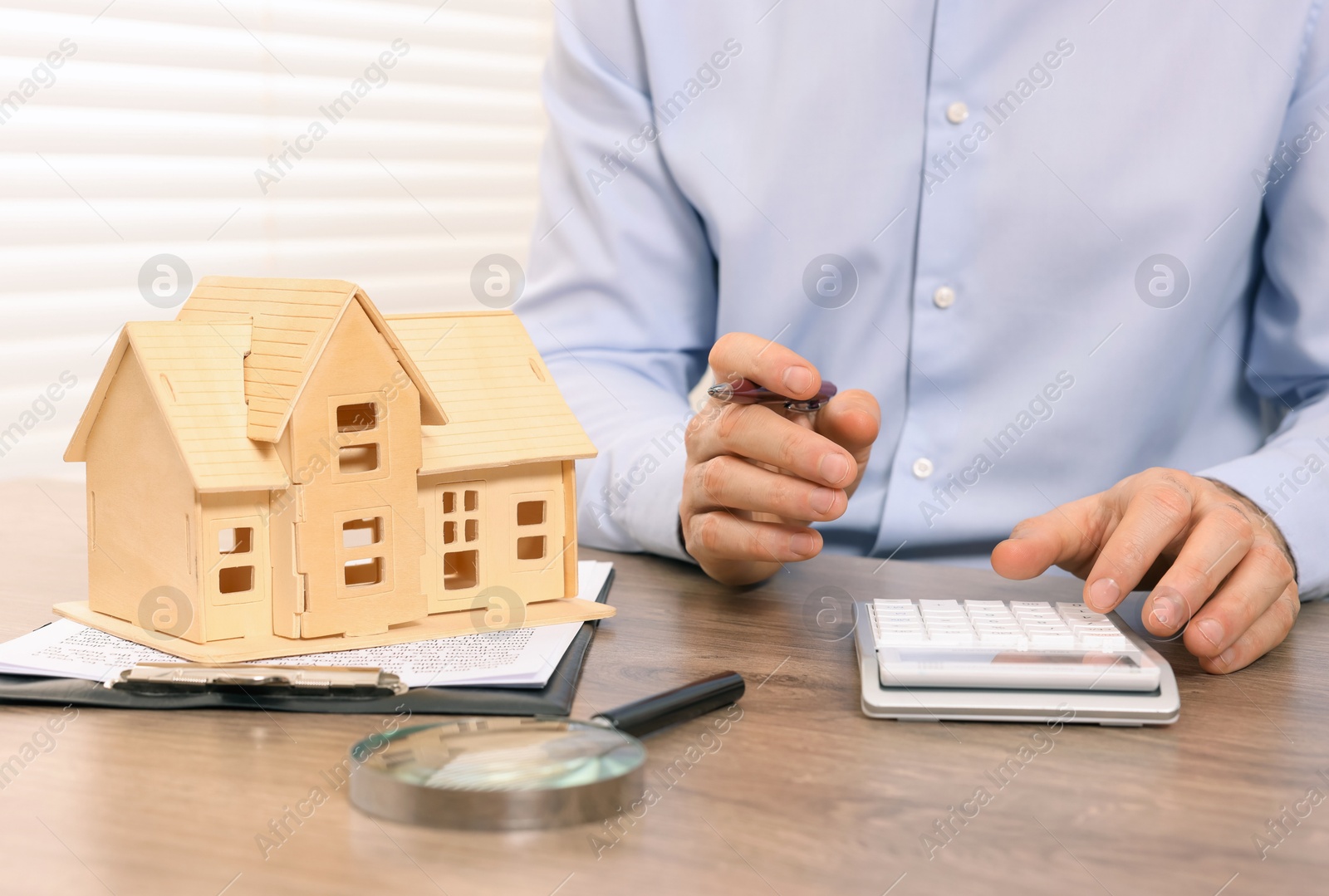 Photo of Real estate agent with calculator at wooden table in office, closeup. Home appraisal