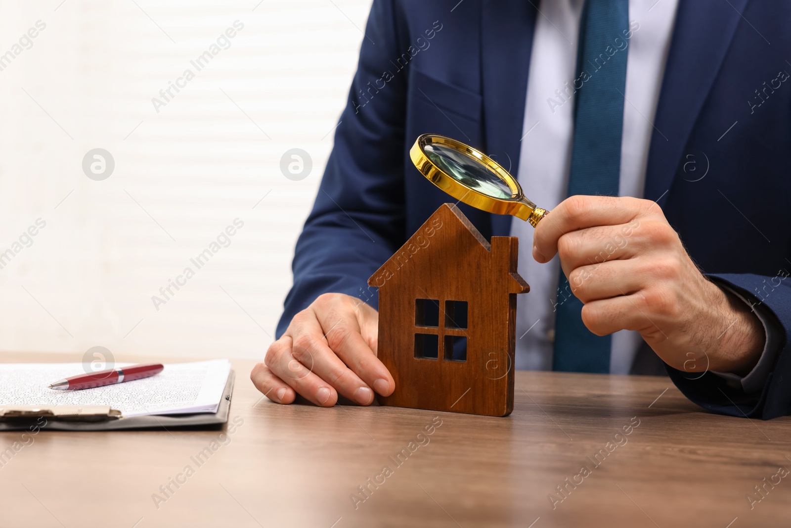 Photo of Real estate agent looking at house figure through magnifying glass at wooden table in office, closeup. Home appraisal