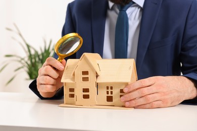 Photo of Real estate agent with house figure and magnifying glass at white table in office, closeup. Home appraisal